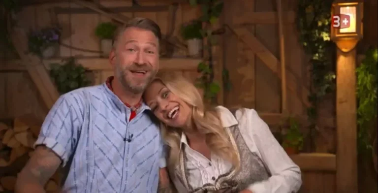 Smiling man and woman leaning together on a rustic wooden set with plants.