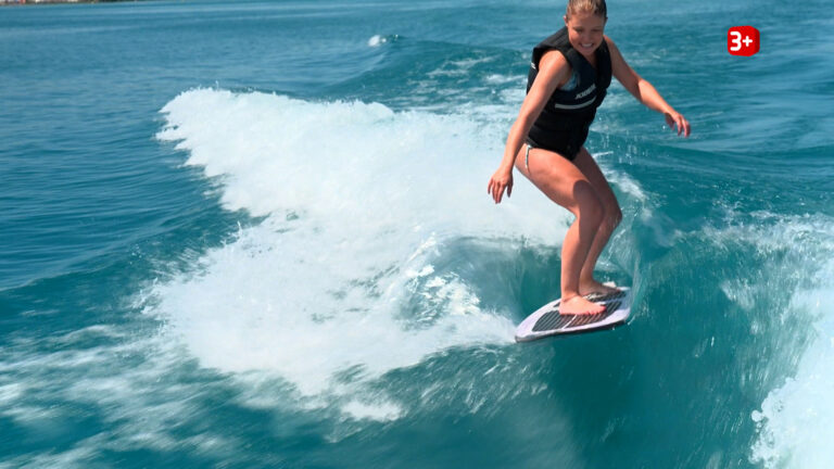 Bauer ledig sucht: Ellie beim Surf-Date mit Dänu (Folge 11) Surfer riding a wave on a blue ocean, wearing a life jacket and balance board rim.